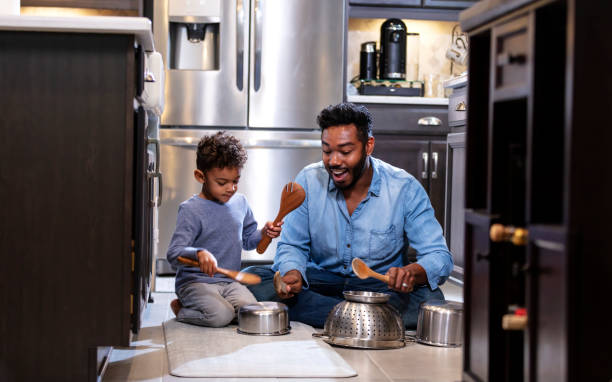 Boy and father on kitchen floor using pots as drums