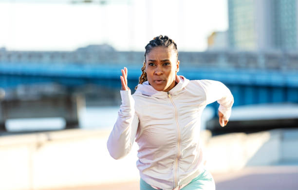 African-American woman on city waterfront, sprinting A mature African-American woman exercising in a city park on the waterfront. She is wearing long sleeved sports clothing, sprinting toward the camera with a serious expression. woman sprint stock pictures, royalty-free photos & images