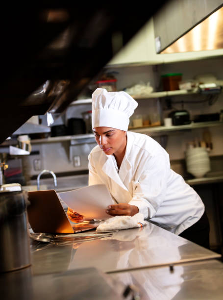 Female chef in commercial kitchen using laptop