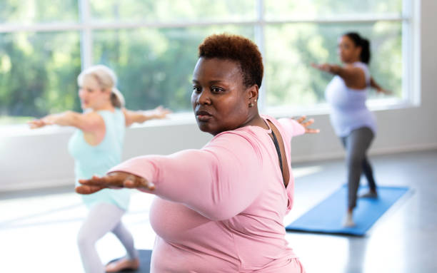 three women taking yoga class, in warrior 2 pose - overweight women serious people imagens e fotografias de stock