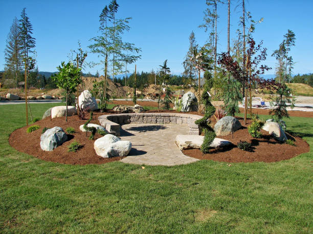 Horseshoe Shaped Deck New horseshoe shape paving stone deck with concrete block  retaining wall built on a mound of dirt filled with boulder - rocks, plants and trees surrounded by a large grass area in form of turf. hardscape photos stock pictures, royalty-free photos & images