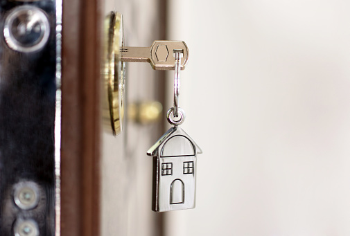 House key on a house shaped silver keyring in the lock of a entrance  door