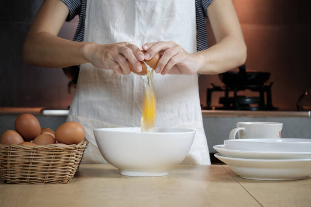istock Female cook in a white apron is cracking an egg in home's kitchen. 1336597111