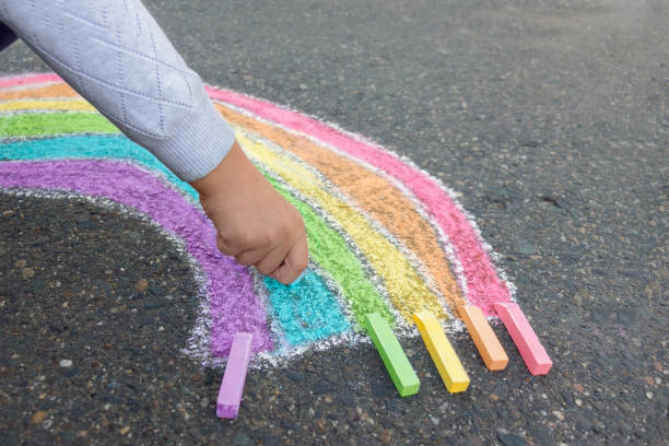 istock Child draws
 rainbow on the asphalt with colored chalk, outdoors. Side view. 1336600387