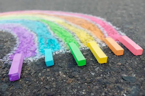 Chalk drawing rainbow colors on the asphalt, children outdoors.