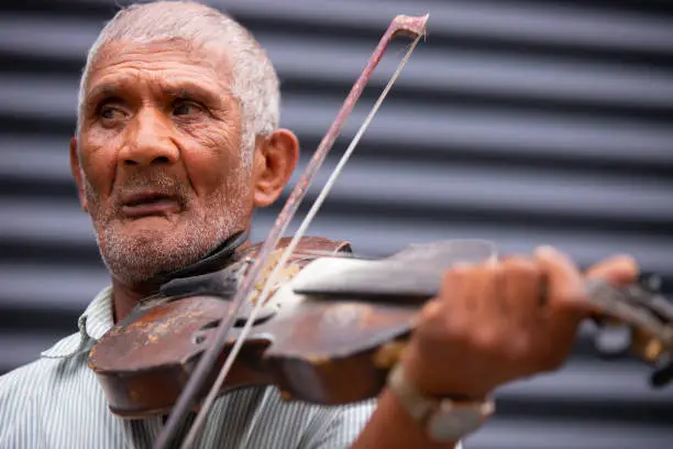 Close up photo of an old gray-hair man using violin playing a wonderful soulful melody outdoors turns his gaze to the side. . High quality photo