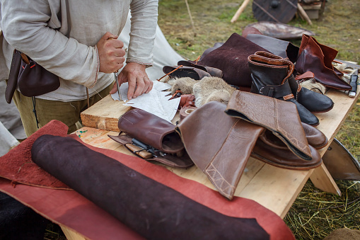 Craft shoemaker demonstrates the process and the products of his work on the festival workshop, tools and leather at cobbler workplace, diy, master of artisanal thing, middle age re-enactment