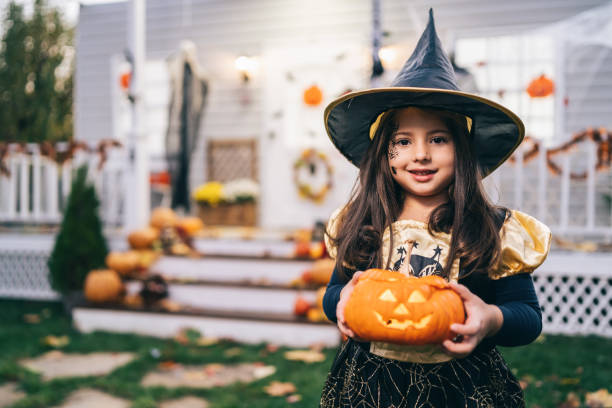 Little girl in witch costume holding Jack-o-Lantern Pumpkins on Halloween trick or treat stock photo