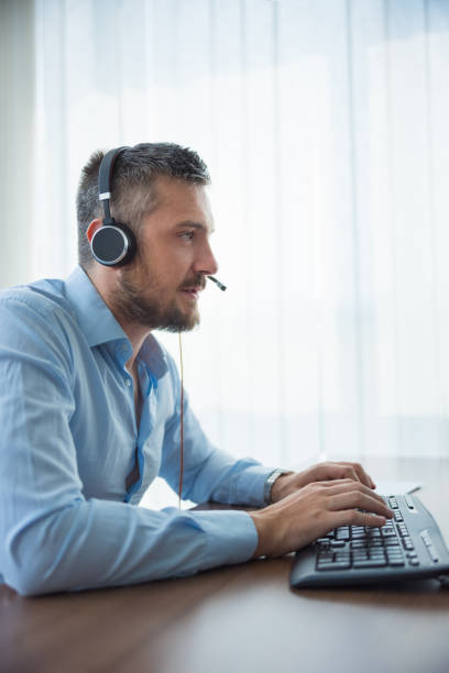 istock Man working at the desk with headset on, typing on computer keyboard 1336609856