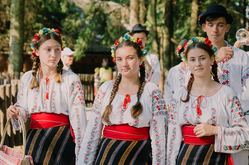 Brasov, Romania - 16 July, 2021: a group of young traditional Romanian dancers and musicians wearing the traditional white costumes with intricate embroidery. They are performing in a local park.