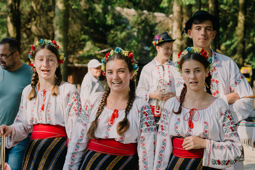 Brasov, Romania - 16 July, 2021: a group of young traditional Romanian dancers and musicians wearing the traditional white costumes with intricate embroidery. They are performing in a local park.