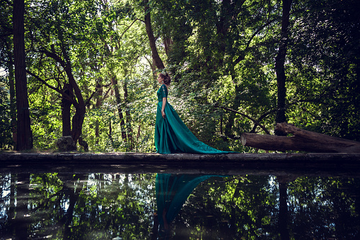 Young woman wearing a green dress explores a magical forest. The idea and concept of fairy tales, magic.