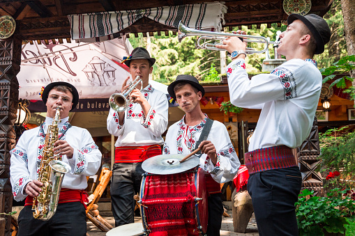 Brasov, Romania - 24 August, 2021: a group of young traditional Romanian dancers and musicians wearing the traditional white costumes with intricate embroidery. They are performing in a local park.