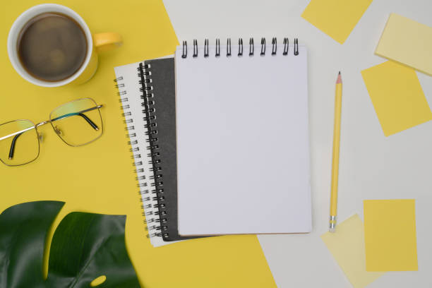 istock Top view empty notebook, glasses, coffee cup and sticky notes on yellow background. 1336621475