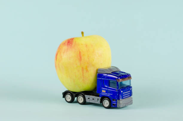istock Toy truck pulling a ripe apple. Blue plastic truck with fruit ag 1336623058