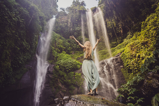Woman in turquoise dress at the Sekumpul waterfalls in jungles on Bali island, Indonesia. Bali Travel Concept.