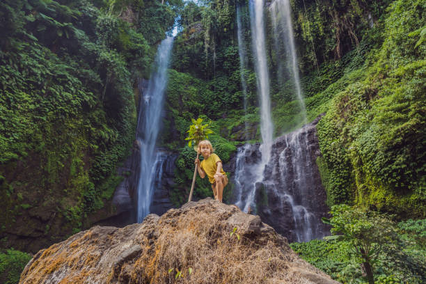 chico lindo representa al rey de la selva contra el telón de fondo de una cascada. concepto de infancia sin artilugios. concepto de viajar con niños. concepto de infancia al aire libre - stream forest river waterfall fotografías e imágenes de stock