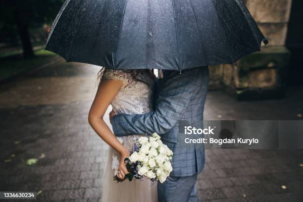 Stylish Bride With Bouquet And Groom Kissing Under Umbrella On Background Of Old Church In Rain Provence Wedding Beautiful Wedding Couple Embracing Under Black Umbrella In Rainy Street Stock Photo - Download Image Now