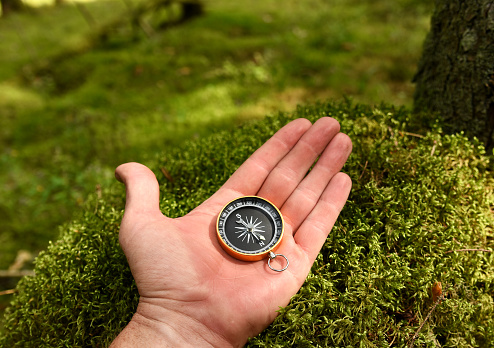 Compass in hand at forest. Tourist compass for orientation on the terrain. Magnetic declination alculator. Historical explorer help. Map reading and land navigation concept. Orient on maps