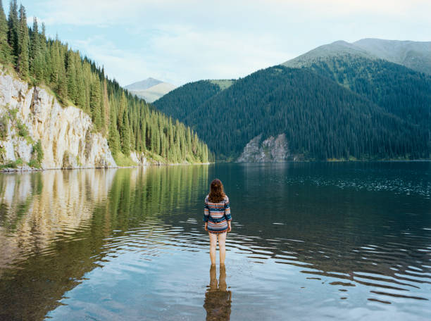 Young Caucasian woman standing in the mountain lake on the background of forest