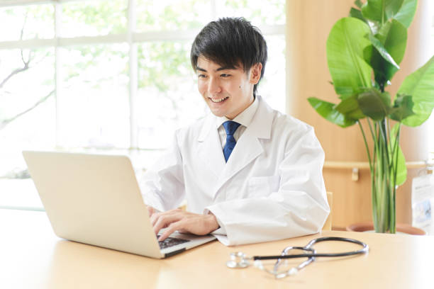 コンピュータ上の情報を調べる男性医師 - オンライン診療 ストックフォトと画像