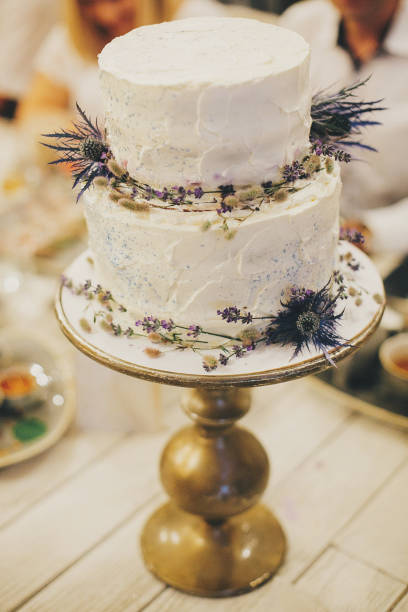 istock Stylish rustic wedding cake with lavender and thistle decor on vintage stand on table at wedding reception in restaurant. Modern beautiful provence wedding cake. Luxury catering at banquets 1336635659