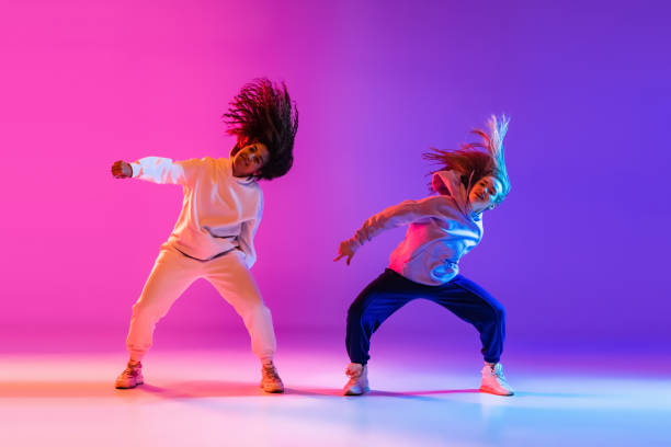 due belle ragazze attive che ballano su sfondo di studio al neon viola sfumato - dancing dancer hip hop jumping foto e immagini stock