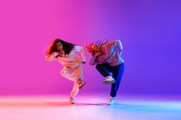 istock Two beautiful active girls dancing on gradient pink purple neon studio background 1336641105
