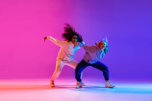 istock Two beautiful active hip-hop girls dancing on gradient pink purple neon studio background 1336641110