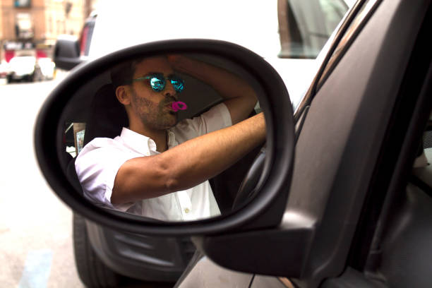 Man inside the car eating a candy with sunglasses and his reflection in the mirror