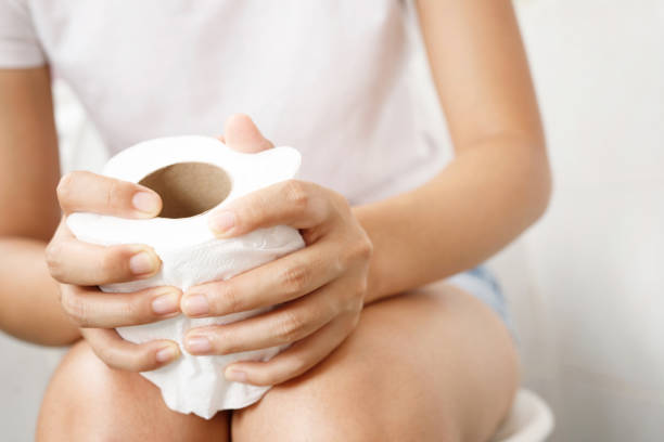 retrato de una mujer sufre de diarrea su estómago doloroso. dolor y problema. sostenga con la mano un rollo de papel de seda frente a la taza del inodoro. estreñimiento en el baño. concepto de higiene, cuidado de la salud. - estreñimiento fotografías e imágenes de stock