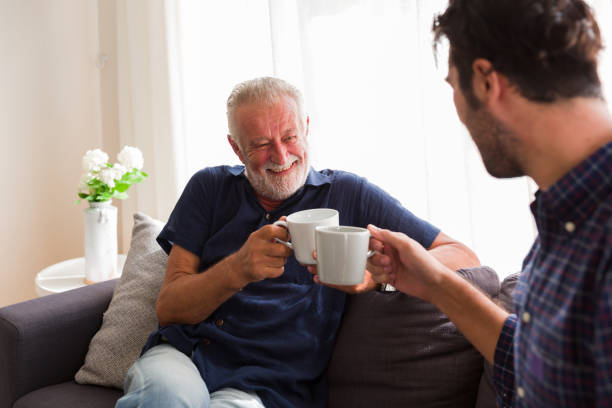 Senior Father and Adult Son smiling and drinking coffee together on sofa at home. Senior Father and Adult Son smiling and drinking coffee together on sofa at home. friends drinking tea stock pictures, royalty-free photos & images