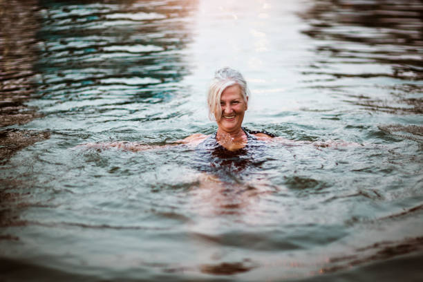 retrato de uma mulher idosa sorridente nadando curtindo a praia. - river swimming women water - fotografias e filmes do acervo