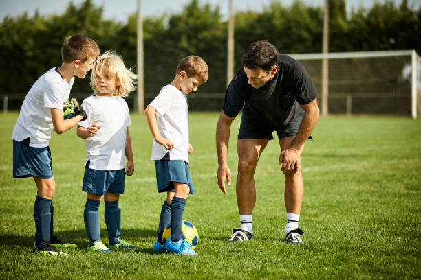 entrenador masculino enseñando fútbol a niños en hierba - soccer child coach childhood fotografías e imágenes de stock