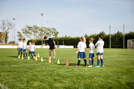 Boy practicing soccer drills. Male coach is training children. They are in playing field.