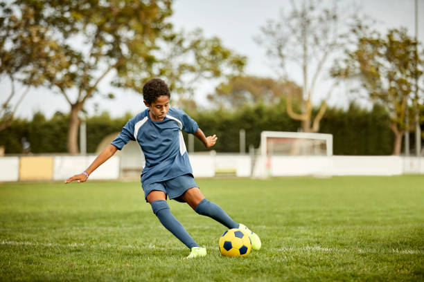 un adolescent donne un coup de pied dans un ballon de football sur le terrain - playing field kids soccer goalie soccer player photos et images de collection