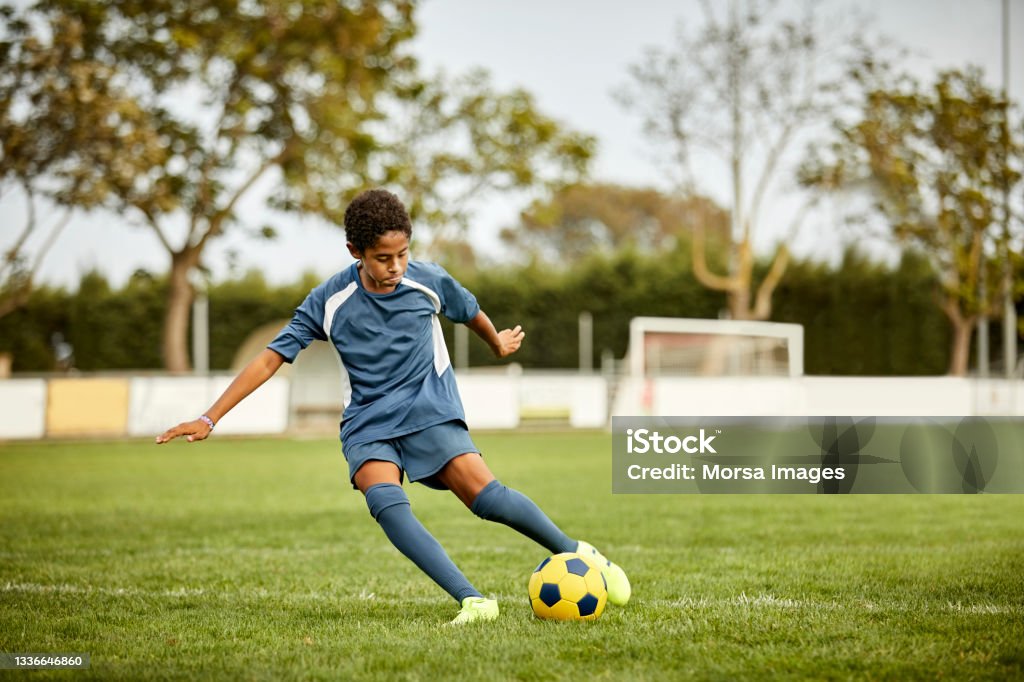 Teenage boy kicking soccer ball in field Teenage boy kicking ball in field. Male practicing soccer on grass. He is in sportswear. Soccer Stock Photo
