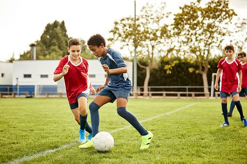 Teenagers practicing soccer in field. Smiling male defending ball during match. They are in uniform.