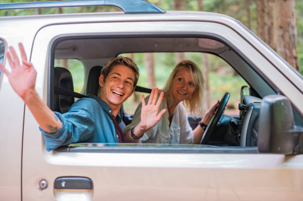 A happy young couple waves goodbye from the car