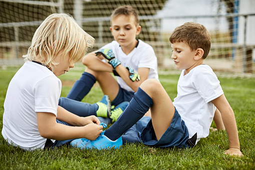 Side view of girl helping boy tie shoe in soccer field
