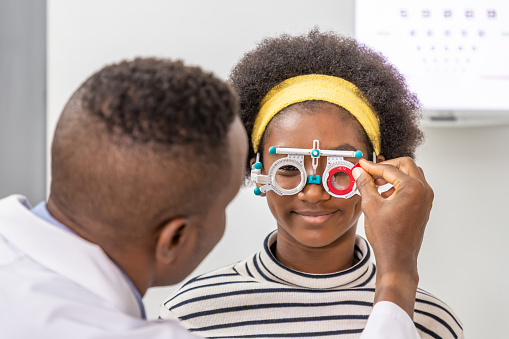 African young woman girl doing eye test checking examination with male man optometrist using trial frame in clinic or optical shop. Eyecare concept.