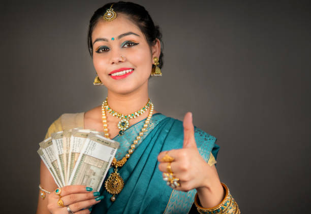 インドのルピー紙幣を持ち、カメラを見てサリの伝統的なインドの女性。 - thumbs up jewelry hinduism women ストックフォトと画像