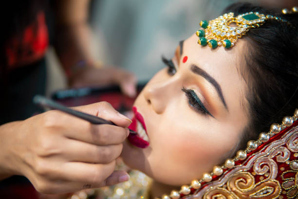 istock Beautiful traditional Indian bride getting ready for her wedding day by makeup artist. 1336649737
