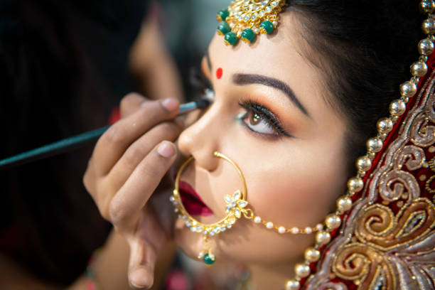 istock Beautiful traditional Indian bride getting ready for her wedding day by makeup artist. 1336649738