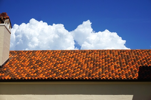 Abstract architecture background with variegated color roof tiles, cottony white clouds and clear blue sky