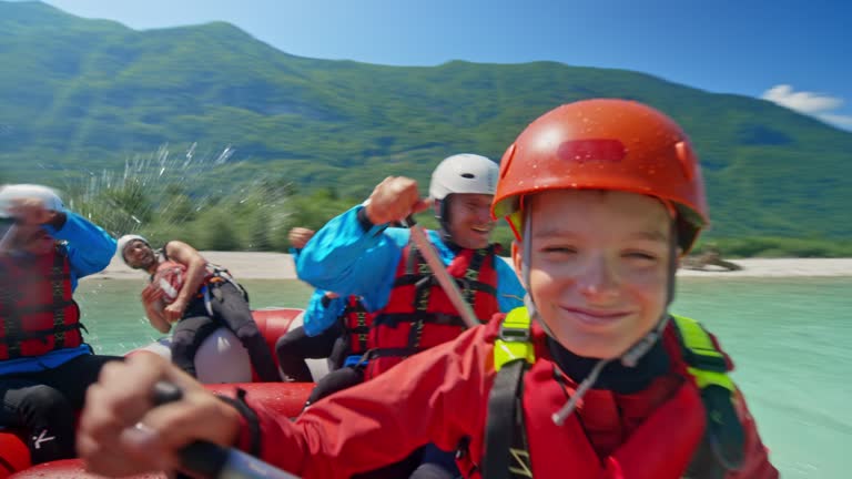 Wide handheld shot of a boy and girl having fun paddling the raft with their family and other members of the rafting team. Shot in Slovenia.
