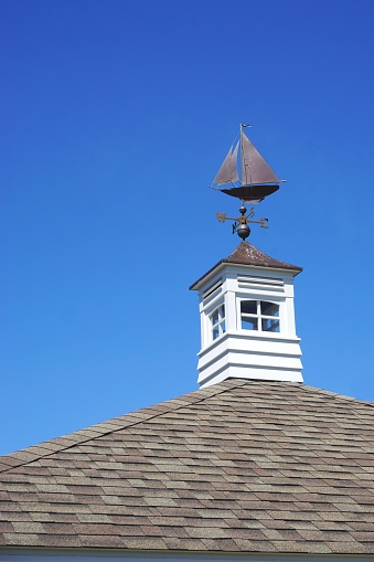 Iconic metal ship weather vane mounted on classic New England rooftop with square white cupola and brilliant blue sunny sky