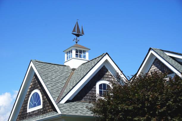 Iconic sailing ship weather vane mounted atop a white cupola on a classic gabled New England rooftop New England-style gabled roof with classic windowed cupola and vintage metal sailboat weather vane cupola stock pictures, royalty-free photos & images
