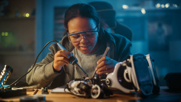 una joven adolescente multiétnica está estudiando electrónica y soldadura de cables y placas de circuitos en su proyecto de robótica de pasatiempo científico. la chica está trabajando en un robot en su habitación. concepto de educación. - robot fotos fotografías e imágenes de stock