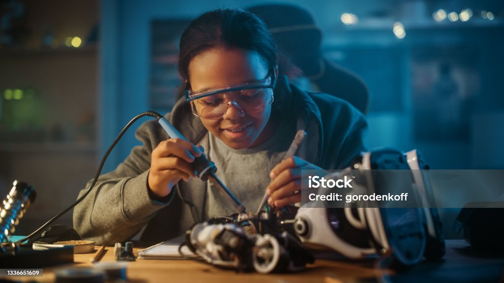 Young Teenage Multiethnic Schoolgirl is Studying Electronics and Soldering Wires and Circuit Boards in Her Science Hobby Robotics Project. Girl is Working on a Robot in Her Room. Education Concept. Child Stock Photo